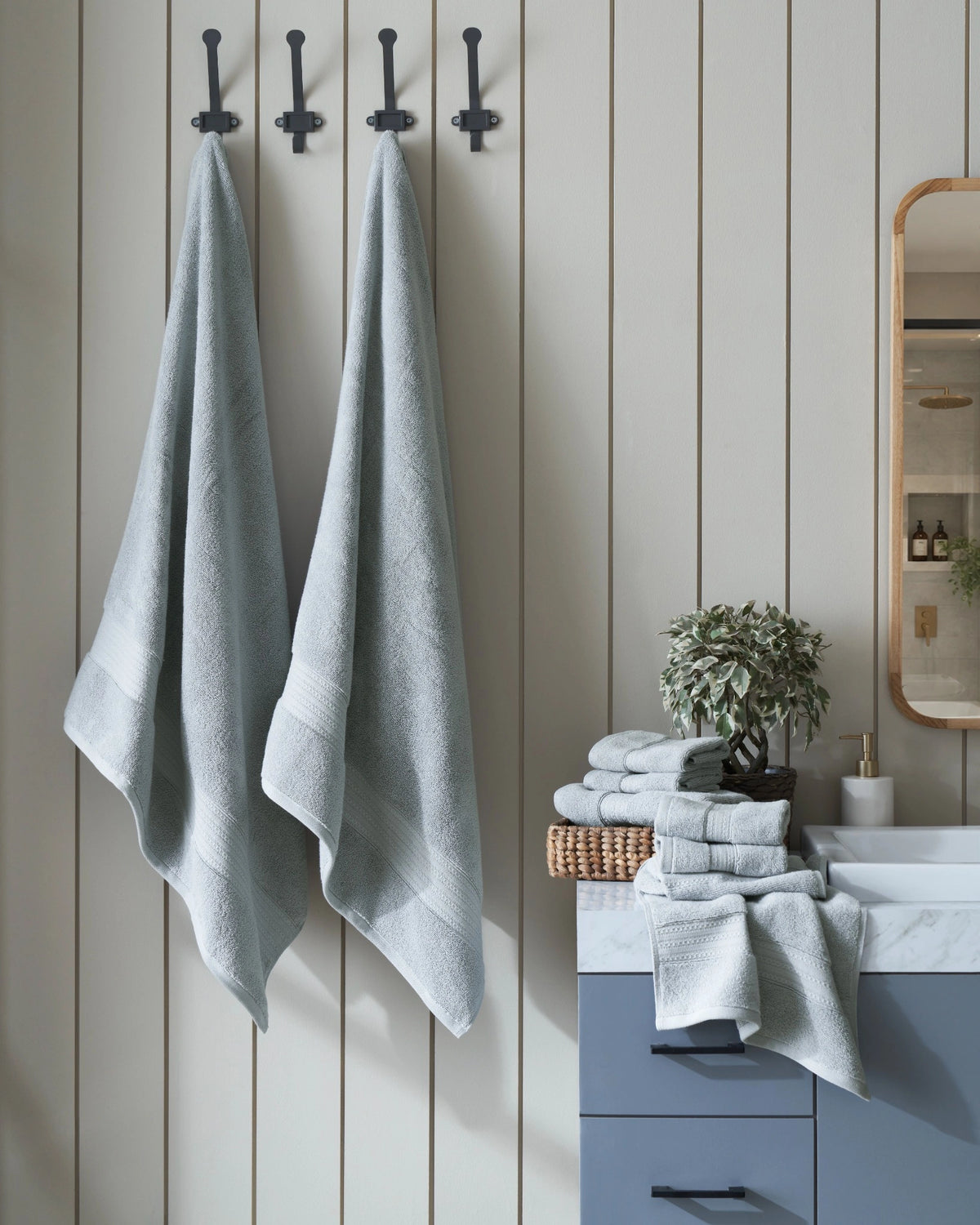 Blue-grey bath towels hanging on wall hooks in a bathroom