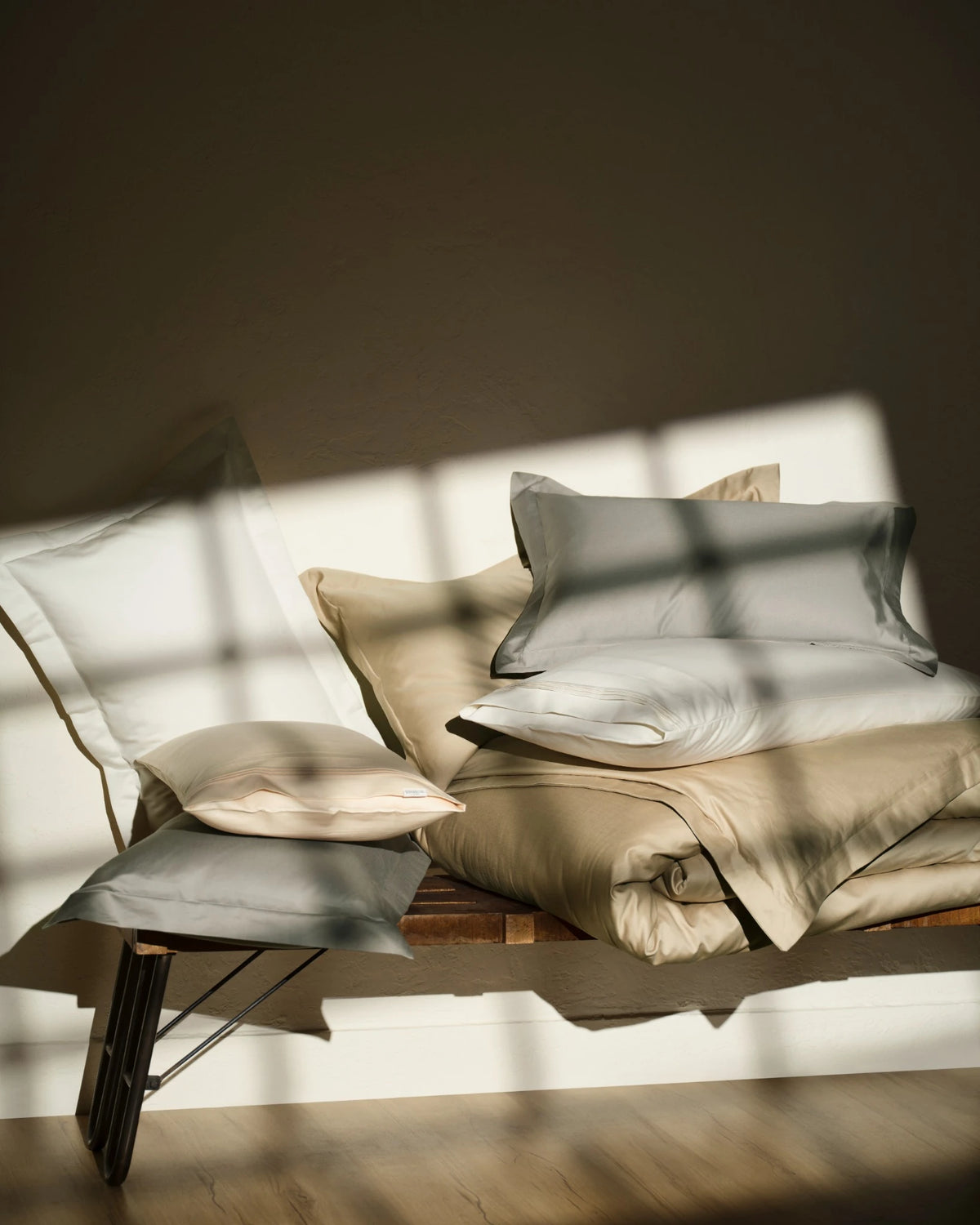 Neutral-toned sheets and pillows on a daybed in soft window light