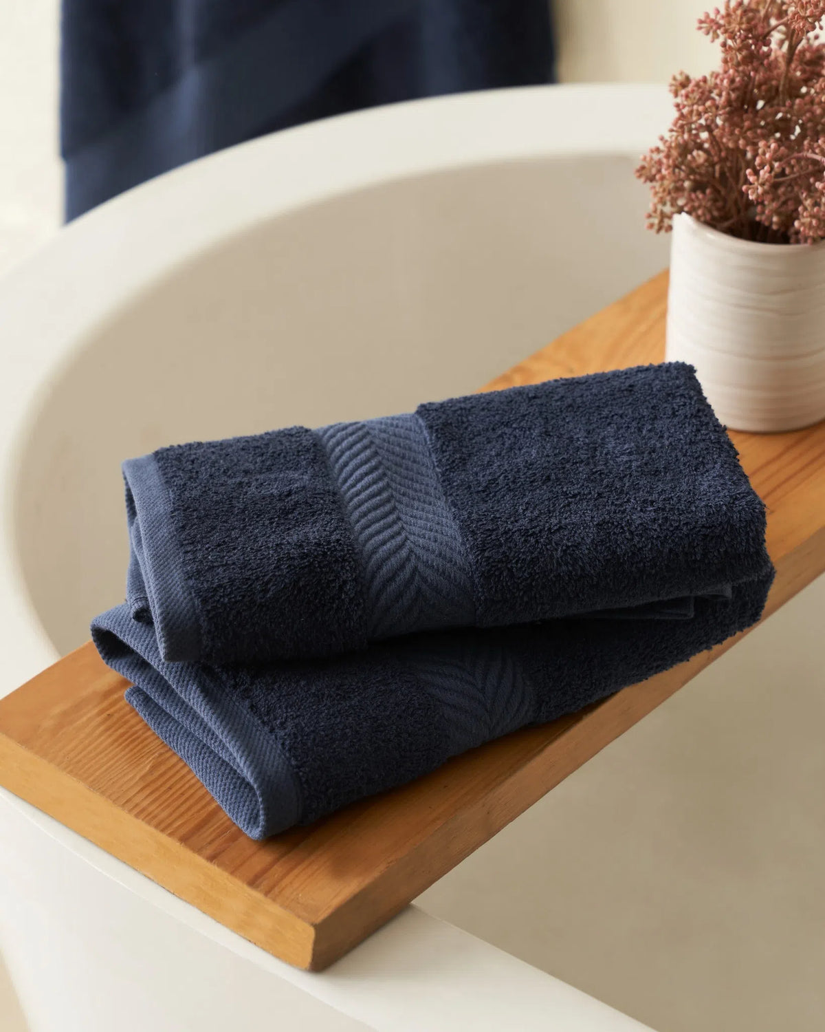 Two folded navy blue hand towels on a wooden bath tray