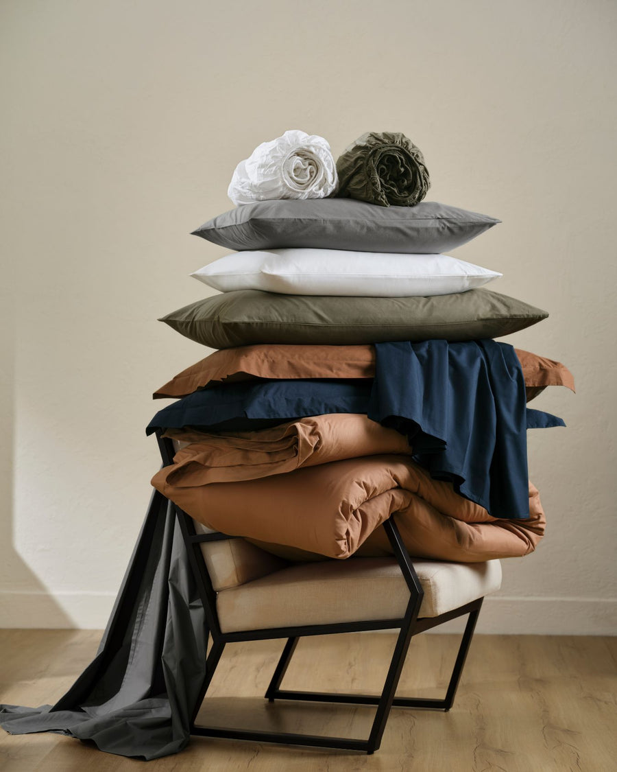 Stack of folded bed linen and pillows in assorted colours on a chair