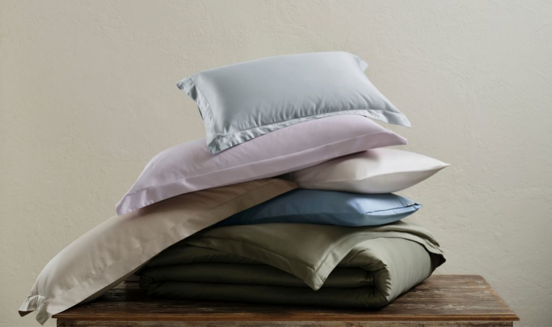 Stack of sateen pillows and sheets in soft pastel colours on a wooden table
